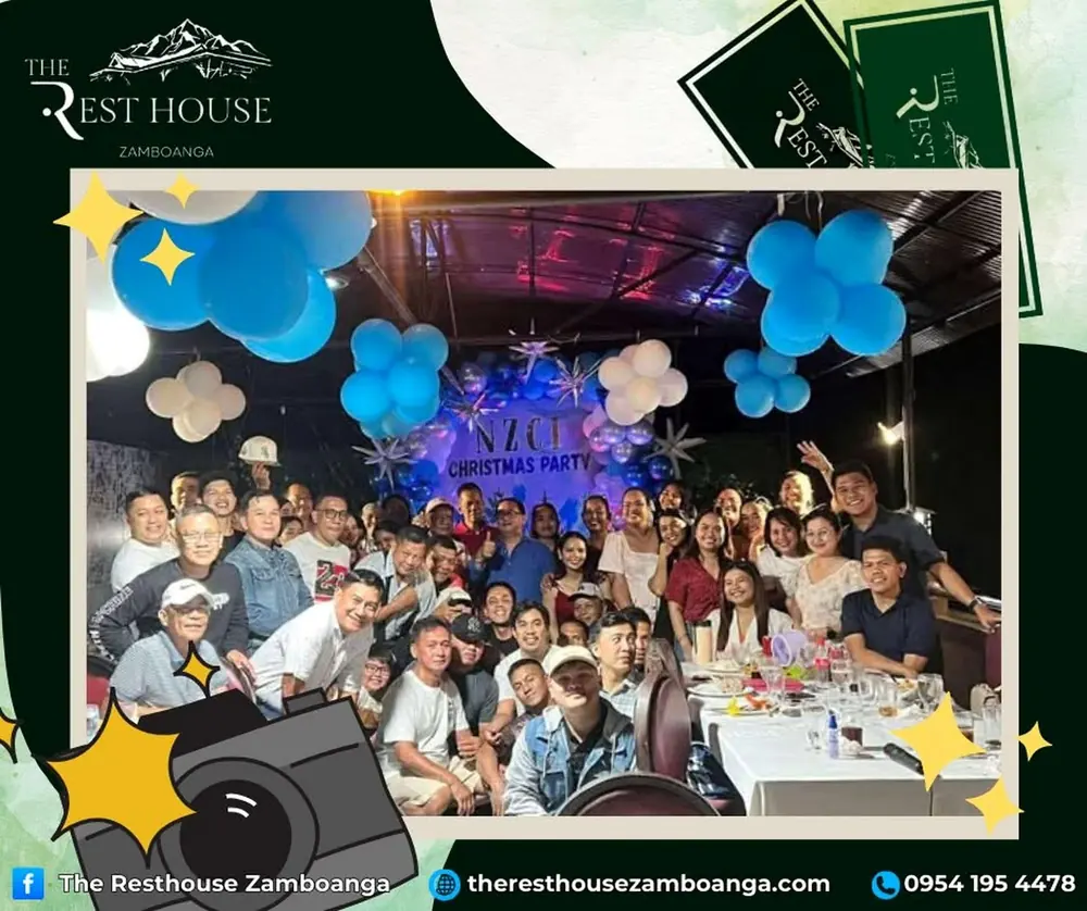 A big group gathered under blue and white balloons at a holiday party
