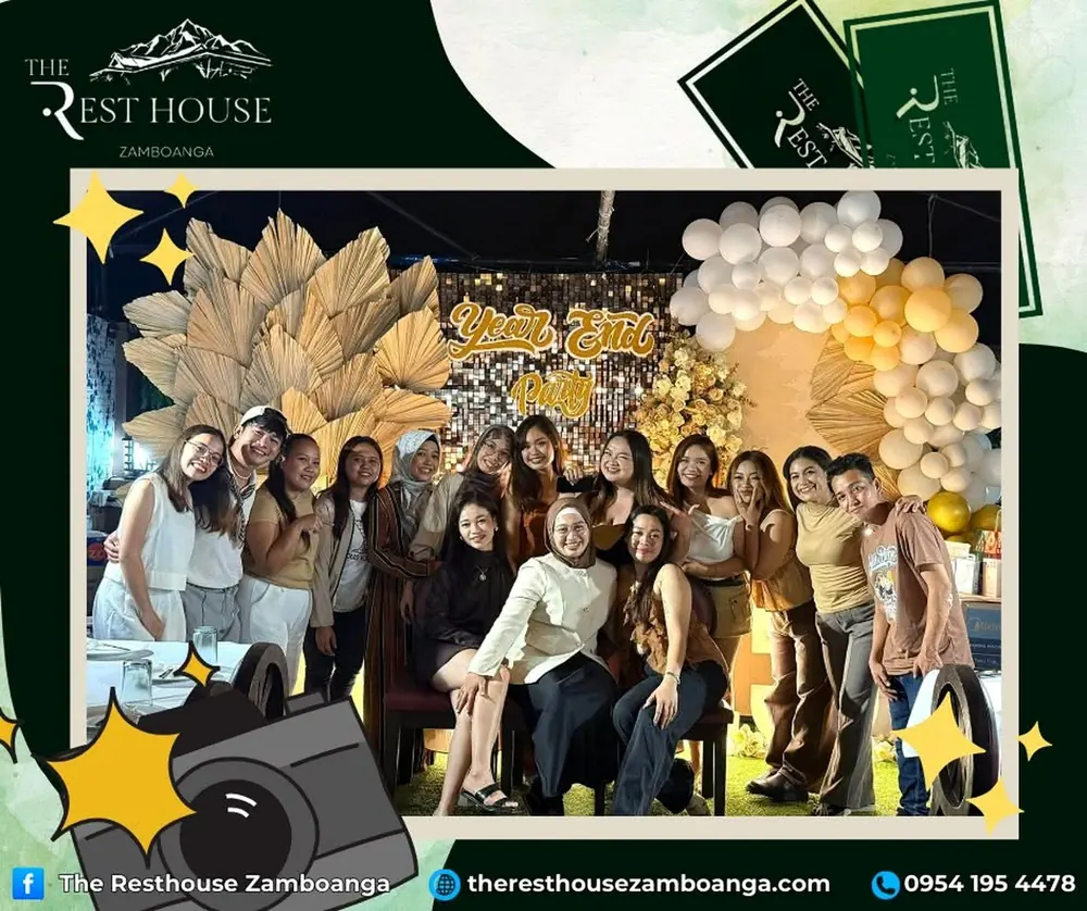 A group of friends smiling in front of a gold and white balloon backdrop at a year-end party