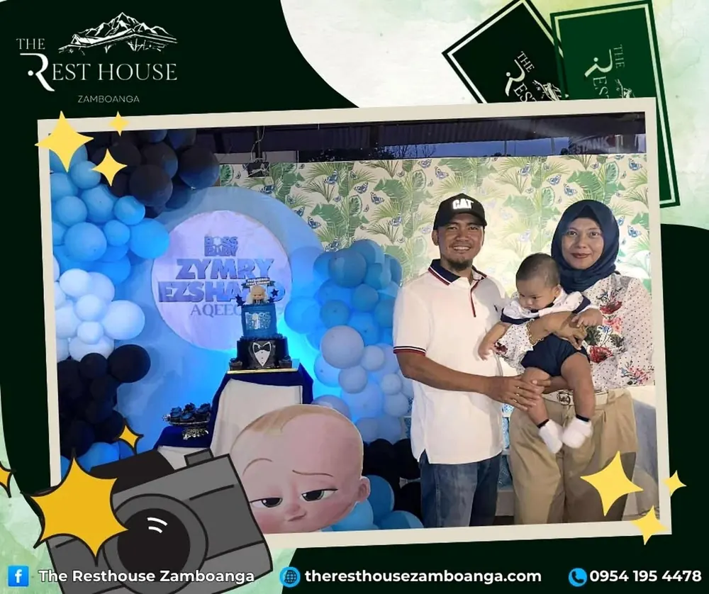 A couple holding their baby in front of a blue balloon and cake display